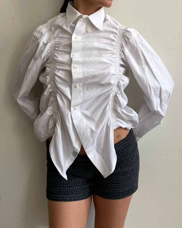 Person wearing a white ruffled long sleeve blouse and black shorts against a plain background